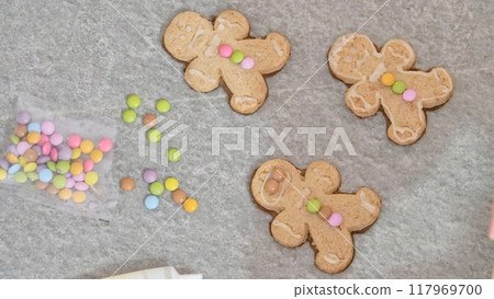 woman's hands decorating a gingerbread man-shaped Christmas cake with white icing and colored caramels, close-up woman's hands decorating a gingerbread man-shaped Christmas cake with white icing and colored caramels, close-up 117969700