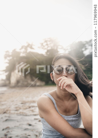 Young Japanese woman wearing sunglasses on a windy sandy beach Young Japanese woman wearing sunglasses on a windy sandy beach 117969948