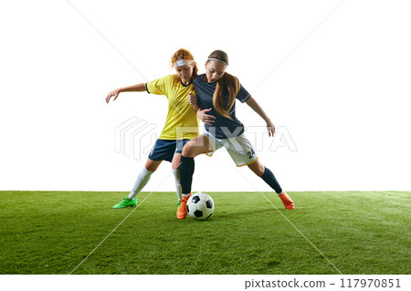 Determined young woman, mid-20s, soccer player, mid-air performing kick, fully focused on ball against white background. 117970851