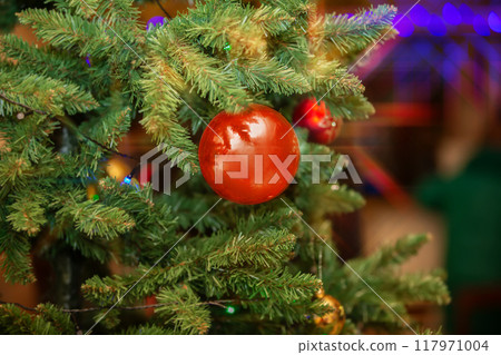 Christmas background. A red ball hangs on the Christmas tree against a background of holiday lights. Christmas background. A red ball hangs on the Christmas tree against a background of holiday lights. 117971004