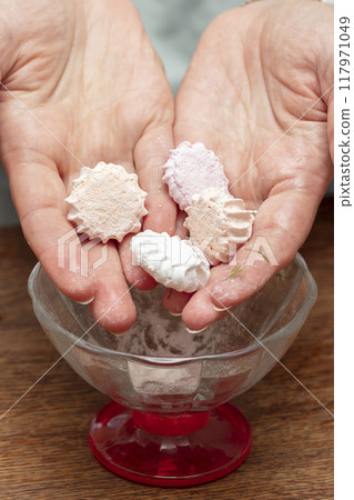 Hands hold several white marshmallow candies. 117971049