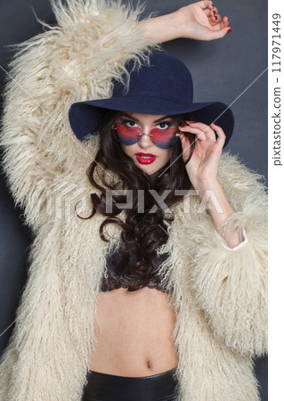 Sensual woman with red lips make-up and long wavy hair wearing blue hat against dark studio wall Sensual woman with red lips make-up and long wavy hair wearing blue hat against dark studio wall 117971449