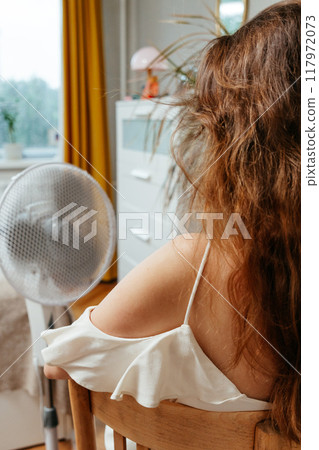 view from back Fan cools Caucasian woman languishing in summer heat. view from back Fan cools Caucasian woman languishing in summer heat. 117972073