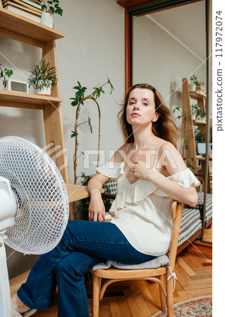 fan cools unhappy Caucasian woman languishing in summer heat. warmed-up experiences hot flashes 117972074