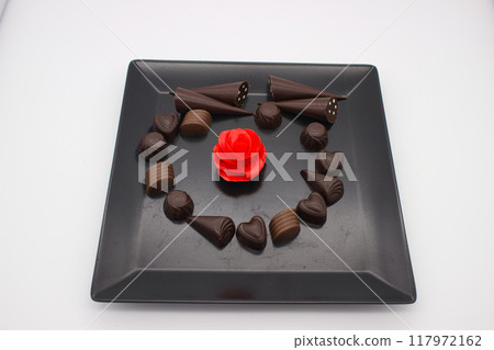 Chocolate Assortment with Red Rose Centerpiece on Black Plate 117972162