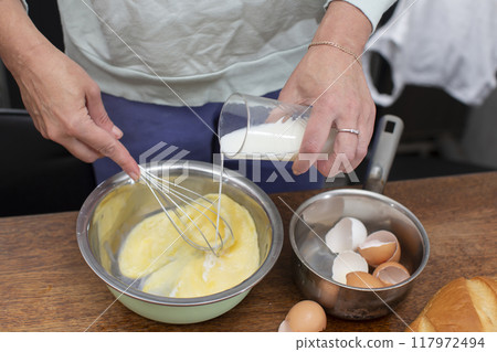 Make an omelet for breakfast. Hands pour milk from a glass into eggs. Make an omelet for breakfast. Hands pour milk from a glass into eggs. 117972494