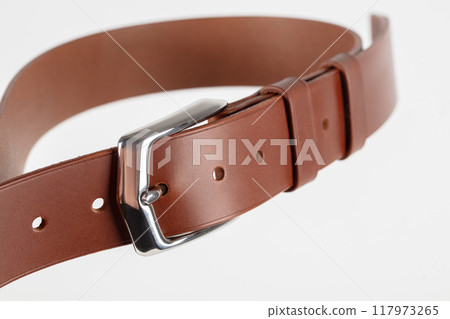 Part of a light brown leather classic belt with a buckle on a gray background. Part of a light brown leather classic belt with a buckle on a gray background. 117973265