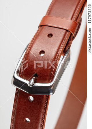 Part of a light brown leather classic belt with a buckle on a gray background. Part of a light brown leather classic belt with a buckle on a gray background. 117973266