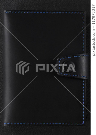 Black leather wallet with blue stitching on a black background. 117973317