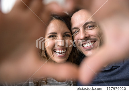 Couple looking at camera through fingers showing symbol of love 117974020