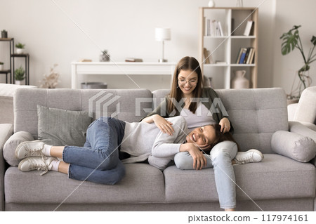 Cheerful mother resting on adolescent daughters laps 117974161