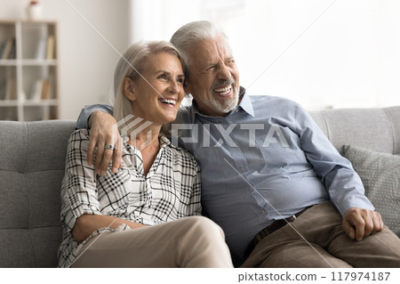 Pretty aged spouses sit on sofa, laughing looking into distance Pretty aged spouses sit on sofa, laughing looking into distance 117974187
