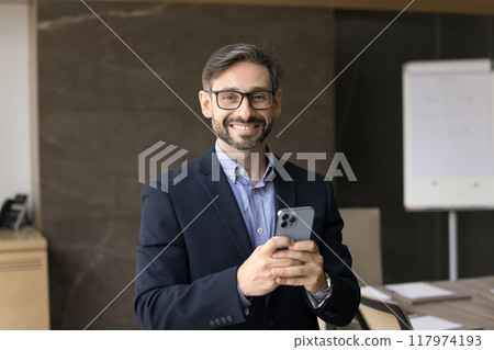 Happy company owner man in glasses using application on phone 117974193