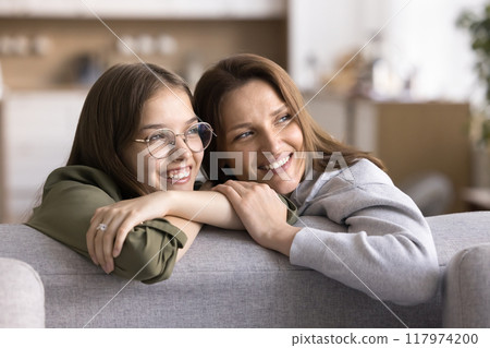 Mother and teen daughter rest on sofa looking away 117974200