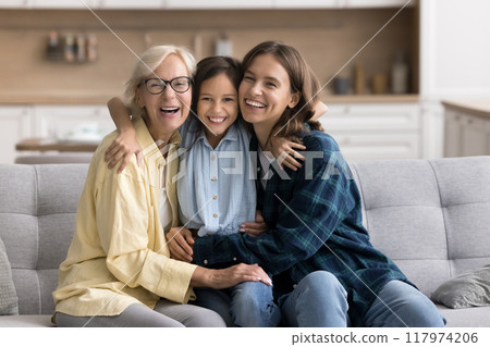 Cheerful kid girl hugging young mom and happy mature grandma Cheerful kid girl hugging young mom and happy mature grandma 117974206