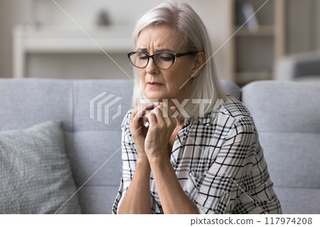 Upset stressed mature woman sitting alone on couch at home Upset stressed mature woman sitting alone on couch at home 117974208