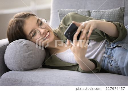 Happy teen girl lying on sofa with smartphone, close up Happy teen girl lying on sofa with smartphone, close up 117974457