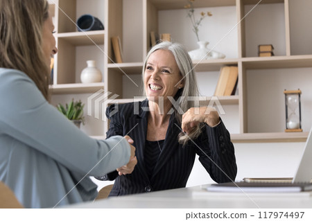 Happy elder businesswoman giving handshake to younger female partner 117974497