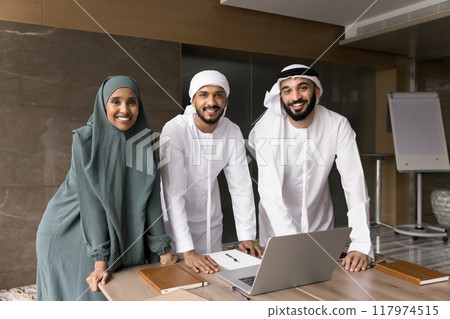 Happy young Arabian business colleagues standing at laptop together Happy young Arabian business colleagues standing at laptop together 117974515