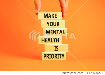 Mental health psychological symbol. Concept words Make your mental health a priority on wooden block. Beautiful orange table orange background. Businessman hand. Psychological mental health concept. 117974650