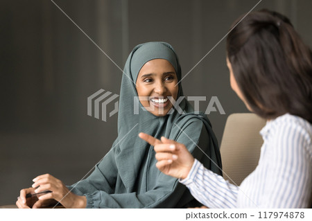 Cheerful Arabian and European business women talking at table 117974878