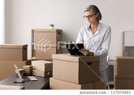 Small business owner working in stockroom filled with cardboard boxes Small business owner working in stockroom filled with cardboard boxes 117974881