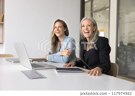 Cheerful female business colleagues sitting at workplace table Cheerful female business colleagues sitting at workplace table 117974982