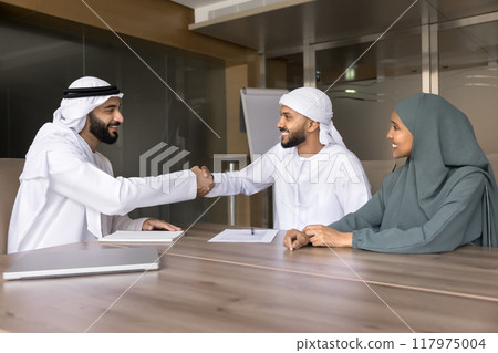 Positive young Arabic business leaders shaking hands at meeting Positive young Arabic business leaders shaking hands at meeting 117975004