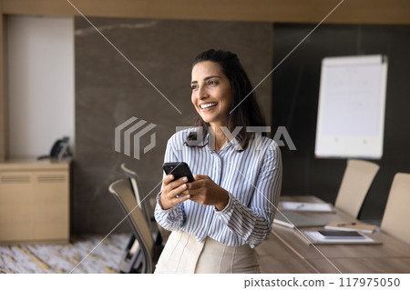 Cheerful dreamy Latin executive woman using mobile phone, digital gadget Cheerful dreamy Latin executive woman using mobile phone, digital gadget 117975050