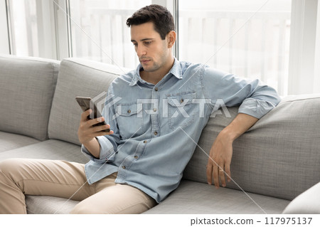 Serious relaxed young Hispanic man typing on mobile phone Serious relaxed young Hispanic man typing on mobile phone 117975137