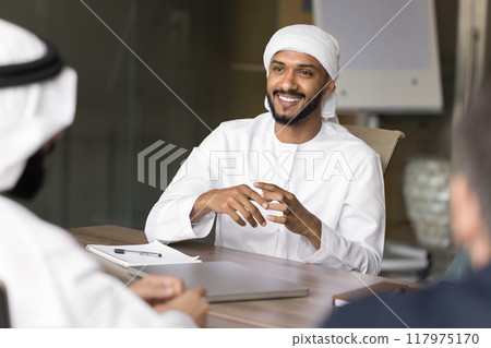 Happy handsome young Arabian business man talking to diverse colleagues Happy handsome young Arabian business man talking to diverse colleagues 117975170