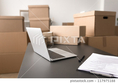 Closeup workspace with laptop, papers on table, boxes in background 117975188