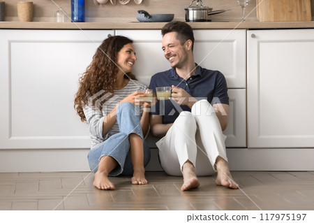 Couple sit on floor in kitchen, holding mugs, celebrate relocation Couple sit on floor in kitchen, holding mugs, celebrate relocation 117975197