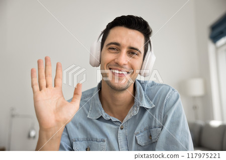 Cheerful Hispanic gadget user man in white headphones waving hello 117975221