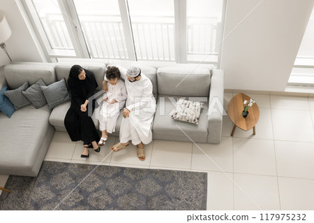 Arab family couple in ethnic clothes hugging kid on sofa 117975232