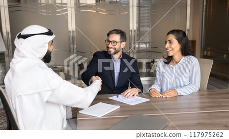 Cheerful European married couple shaking hands with Arabian business consultant Cheerful European married couple shaking hands with Arabian business consultant 117975262