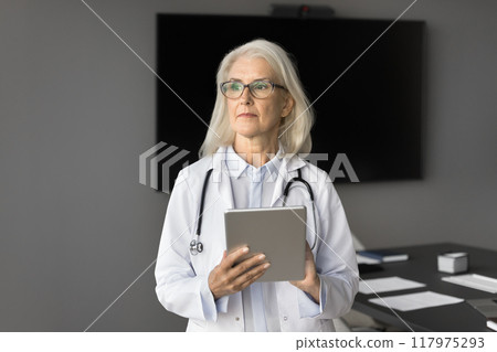 Pensive middle-aged therapist holding tablet looking into distance Pensive middle-aged therapist holding tablet looking into distance 117975293
