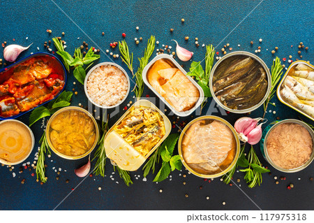 Different open tin cans with canned fish like salmon, mackerel, sprat, sardine, tuna, and herring, among spices and herbs on a blue background Different open tin cans with canned fish like salmon, mackerel, sprat, sardine, tuna, and herring, among spices and herbs on a blue background 117975318