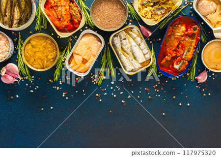 Different open tin cans with canned fish like salmon, mackerel, sprat, sardine, tuna, and herring, among spices and herbs on a blue background, viewed from the top Different open tin cans with canned fish like salmon, mackerel, sprat, sardine, tuna, and herring, among spices and herbs on a blue background, viewed from the top 117975320