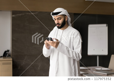 Focused young Arabic businessman typing on smartphone Focused young Arabic businessman typing on smartphone 117975352