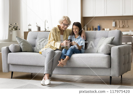 Positive senior grandma and cheerful kid girl using online application 117975420