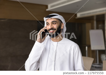 Cheerful handsome young Arabian CEO man talking on cellphone Cheerful handsome young Arabian CEO man talking on cellphone 117975550