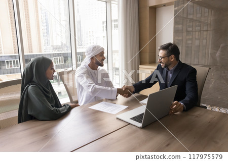 Positive European businessman shaking hands with Arab business partner Positive European businessman shaking hands with Arab business partner 117975579