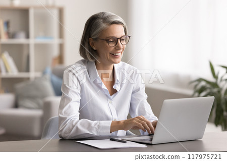 Smiling mature business woman work on laptop at home Smiling mature business woman work on laptop at home 117975721