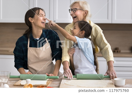 Cheerful girl touching face of cooking and laughing mom Cheerful girl touching face of cooking and laughing mom 117975760