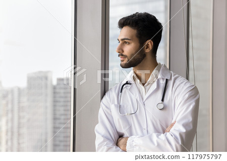 Doctor in coat standing near window, gazing thoughtfully into distance Doctor in coat standing near window, gazing thoughtfully into distance 117975797