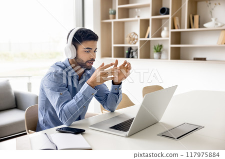 Serious young freelance businessman in headphones talking on video call Serious young freelance businessman in headphones talking on video call 117975884