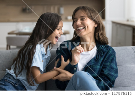 Excited active kid tickling cheerful laughing young mom on sofa 117976115