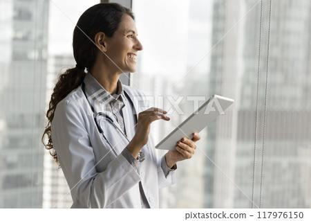 Therapist holding tablet looking out window, feels satisfied with workday 117976150