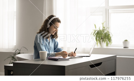Focused young woman in headphones studying at home using laptop 117976255